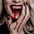 Close up image of a woman dressed in a vampire costume with fake blood dripping from her fangs and on her hand.