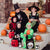 Image of kids sitting on a front porch dressed in Halloween costumes, with Halloween decorations behind them, holding treat bags and wearing accessories.