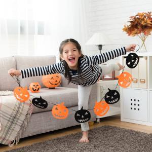 Image of a girl decorating for Halloween with a child friendly pumpkin bunting decoration in her hands.