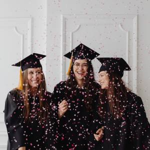 Image of three girls in graduation caps and gowns with confetti